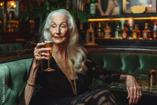 Perfect at any age. Gorgeous old lady in black dress holding a glass of white sparkling wine at dinner party of high society. Perfect make-up and hairdo. Indoor shot