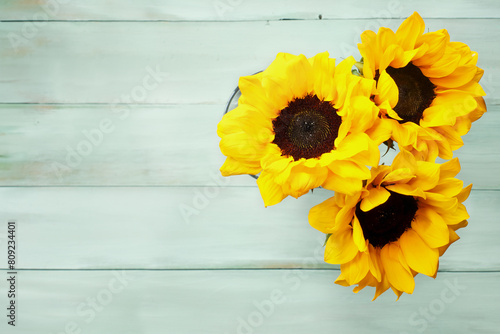 Top view of a bouquet of three yellow sunflowers in a glass vase over a rustic painted table. Copy space available. Flat lay.