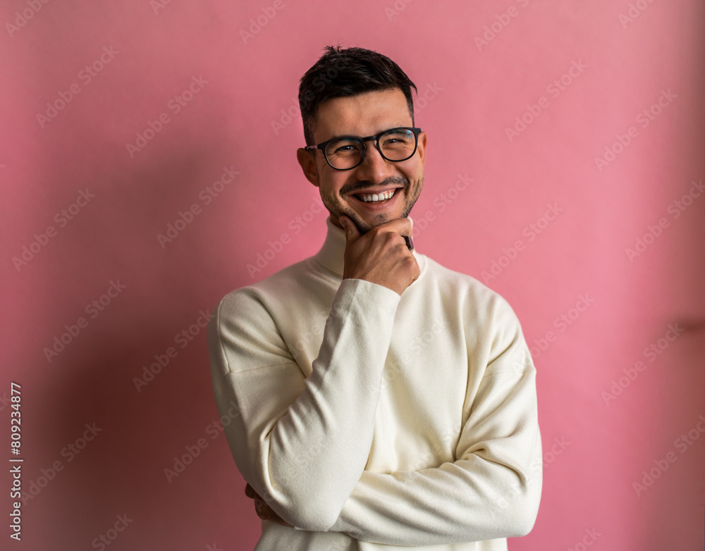 Fototapeta premium A man with glasses and a white sweater stands in front of a pink wall, smiling