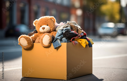 Donation box with used clothes and bear on light nature blurred photo