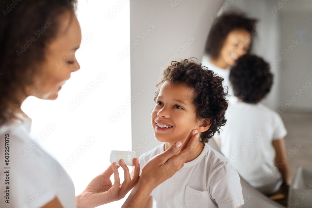 African American mother tenderly applies sunscreen to her child cheerful face, ensuring protection from the suns rays. Both are dressed in casual white attire, reflecting a carefree, sunny day. African American mother tenderly applies sunscreen to her child cheerful face, ensuring protection from the suns rays. Both are dressed in casual white attire, reflecting a carefree, sunny day.