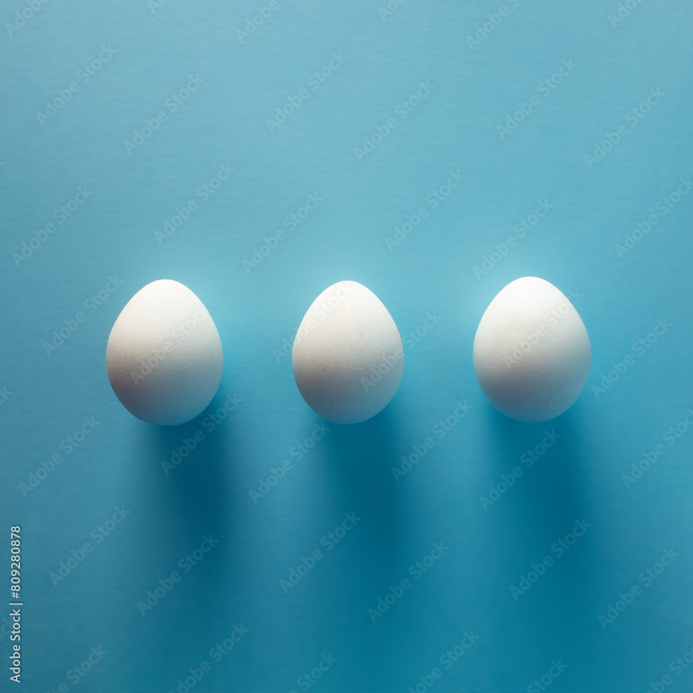 Three white eggs on blue background - flat lay Three white eggs on blue background - flat lay