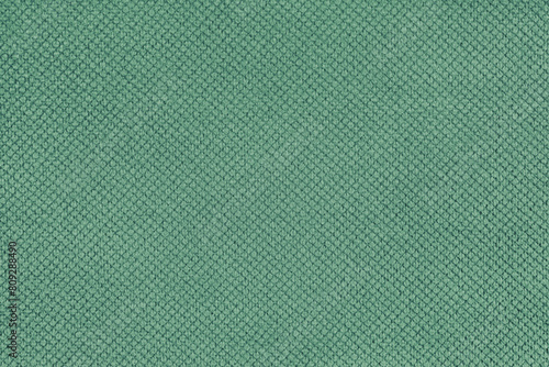 Plain green velor upholstery fabric, jacquard with fine diamond texture background. Close up, macro cloth textile surface. Wallpaper, backdrop with copy space