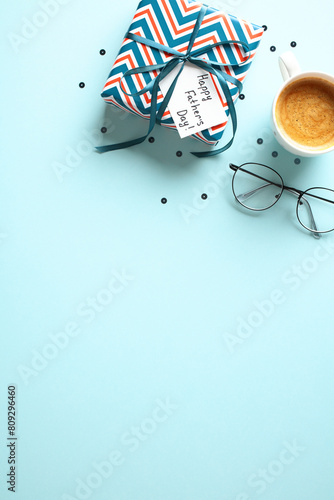 Happy Fathers Day gift box, coffee cup, glasses on pastel blue background. Flat lay, top view, copy space.