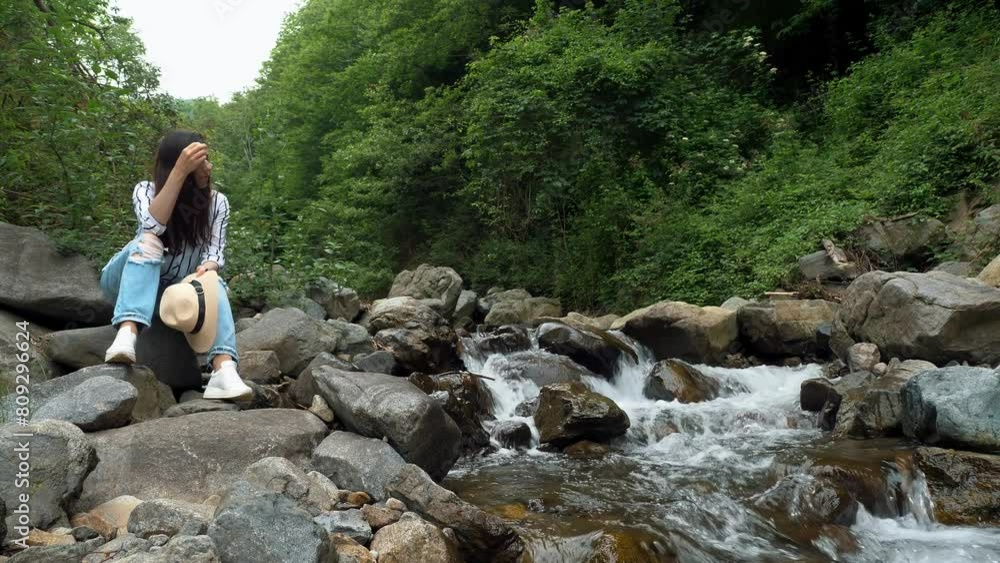 A girl relaxing in the mountains by a mountain river. Tourism, hiking, and leisure. Summer in the Alps. A girl relaxing in the mountains by a mountain river. Tourism, hiking, and leisure. Summer in the Alps.