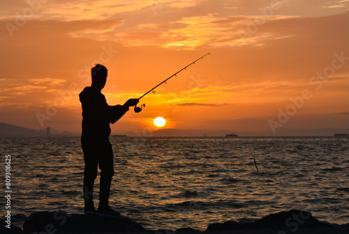 Fisherman casting a fishing line at sunset, silhouette 