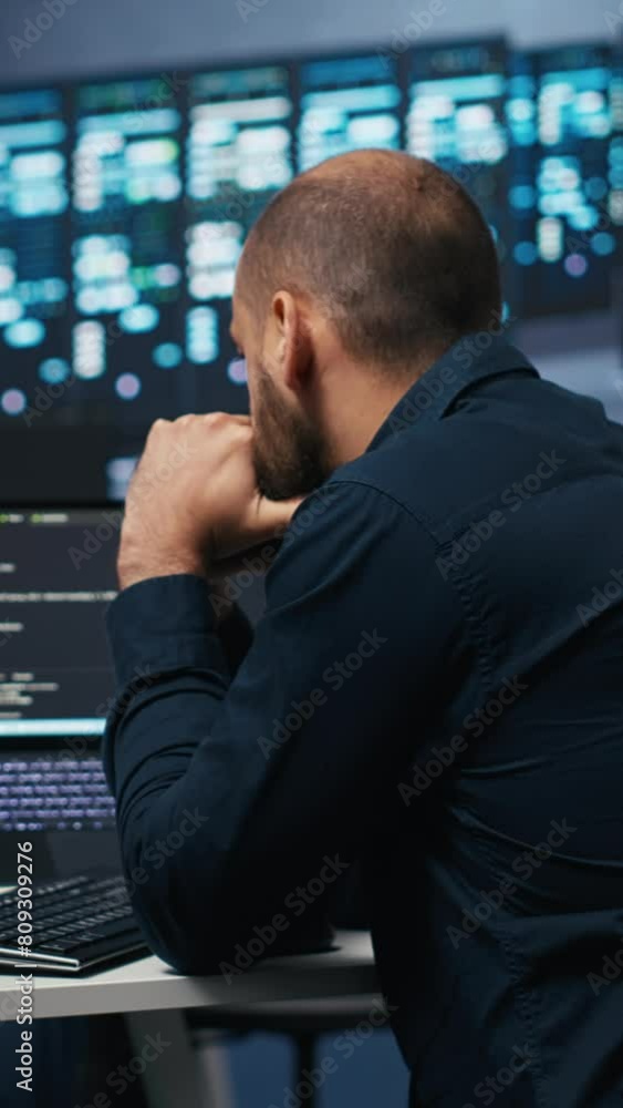 Vertical video Man in server room typing code on laptop and PC, ensuring data remains shielded from threats. IT expert using notebook and computer to protect supercomputers against unauthorized access Vertical video Man in server room typing code on laptop and PC, ensuring data remains shielded from threats. IT expert using notebook and computer to protect supercomputers against unauthorized access