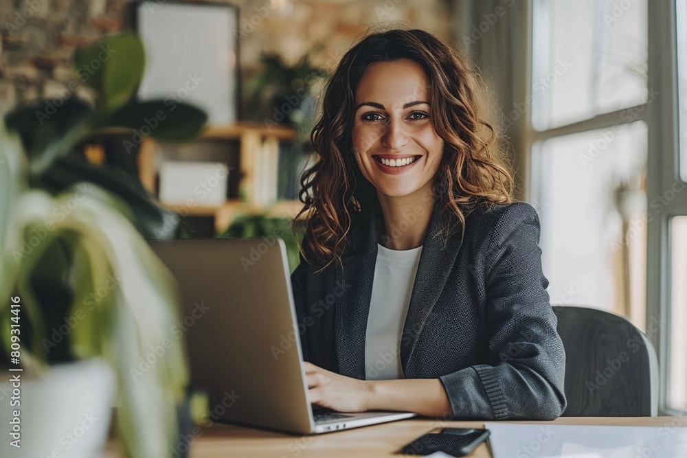 Fototapeta premium Smiling businesswoman using laptop at desk in workplace