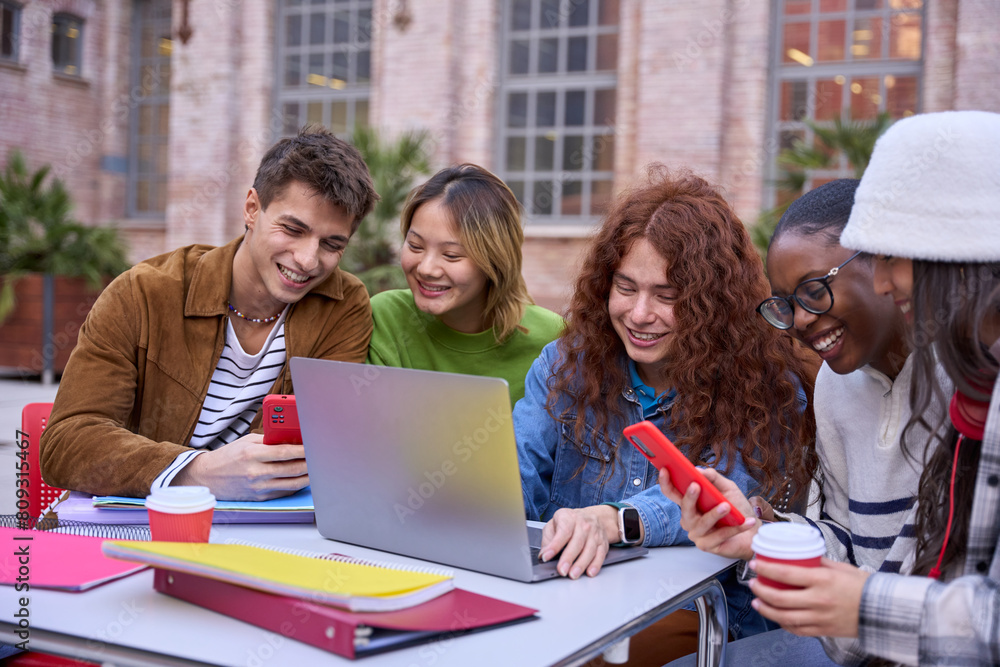 Group of happy multiracial students meeting to study together at university campus using laptop and phone. Generation z smiling people sitting at table and talk to work on creative assignment outdoor Group of happy multiracial students meeting to study together at university campus using laptop and phone. Generation z smiling people sitting at table and talk to work on creative assignment outdoor