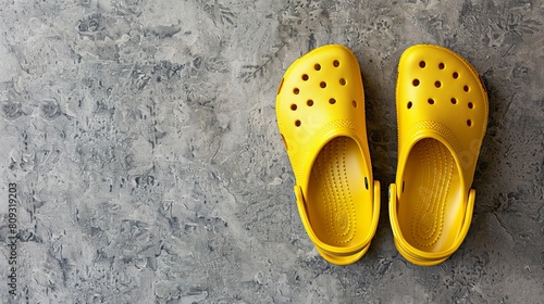 Bright yellow Crocs footwear positioned on a grey background, accompanied by copy space, reflecting a bright and trendy beach shoe perfect for summer vacations photo