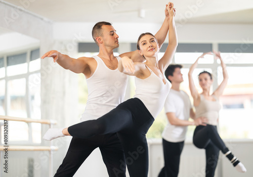 Confident concentrated man, ballet dancer, providing support of graceful female partner in challenging movements, during group rehearsal in vibrant choreography studio