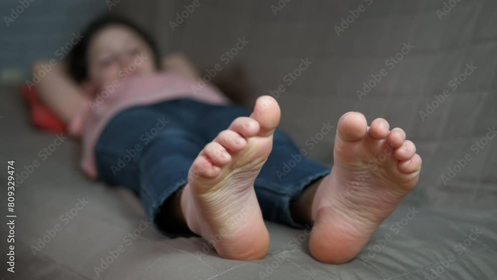 Playful bare child legs on sofa. A playful little girl relax on the sofa with bare feet. A concept of joyful childhood time.