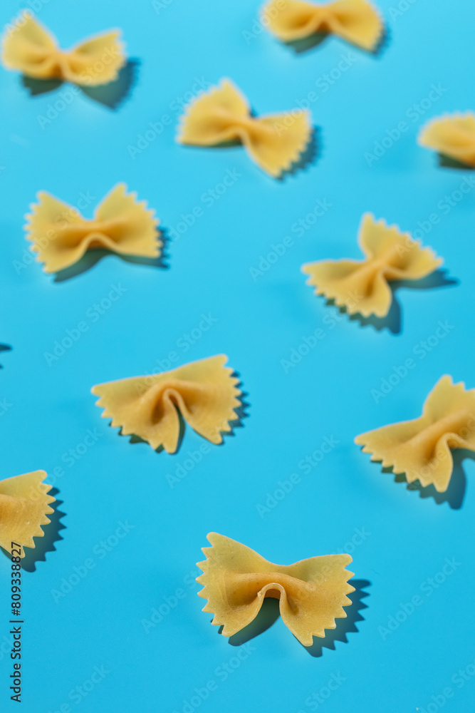 Naklejka premium Uncooked bow tie pasta, farfalle scattered on a blue background in a decorative pattern