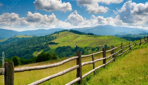 wooden fence on the meadow mountainous rural landscape of transcarpathia ukraine in summer carpathian countryside with forested rolling hill beneath a blue sky with white fluffy clouds