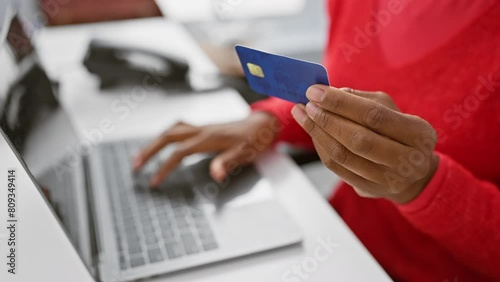 African american woman in red sweater using credit card with laptop in office setting photo