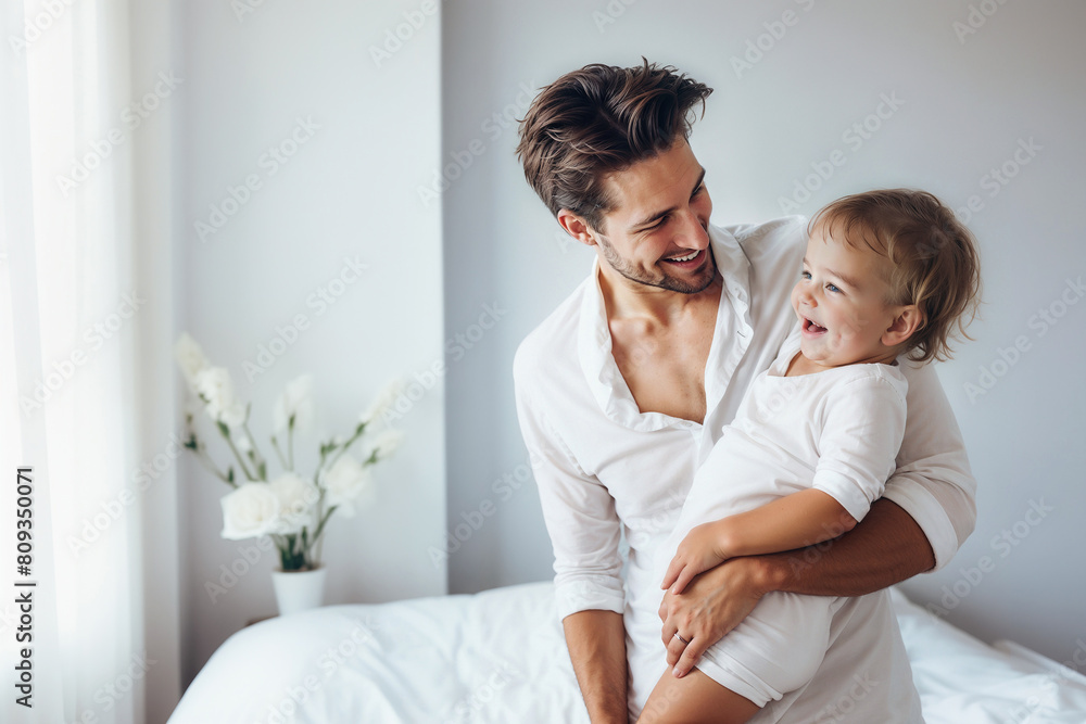 Lifestyle father holding his laughing baby stands near the window in white bedroom. Lifestyle father holding his laughing baby stands near the window in white bedroom.