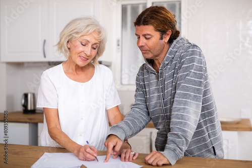 Aged woman and man sign documents sitting in luxury room interior