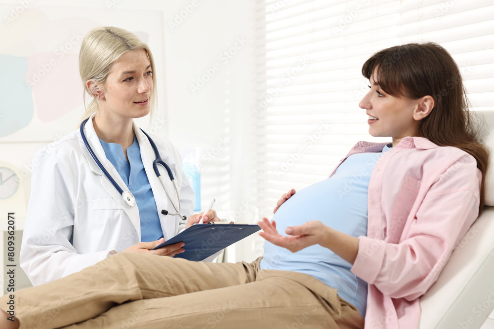 Doctor with clipboard consulting smiling pregnant patient in clinic Doctor with clipboard consulting smiling pregnant patient in clinic