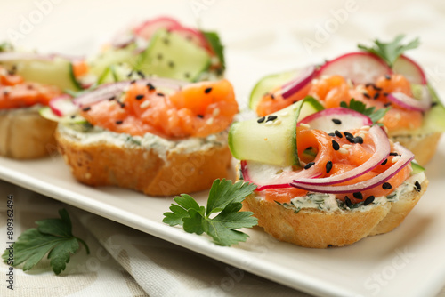 Tasty canapes with salmon served on white wooden table, closeup