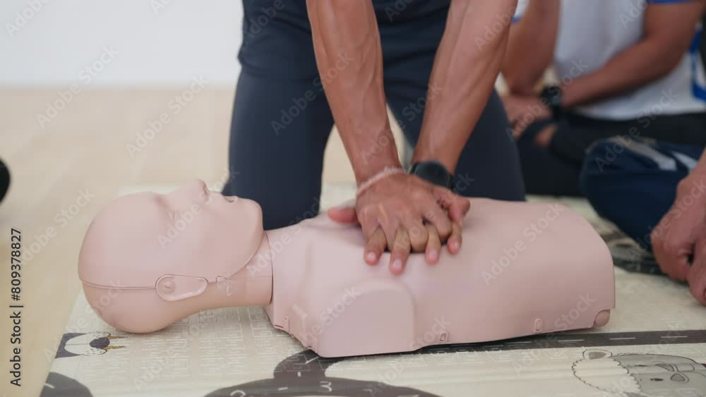 A man is performing CPR on a mannequin. The scene is instructional and ...