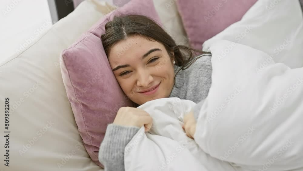 A joyful young hispanic woman embraces a pillow in a cozy bedroom setting, radiating relaxation and happiness. A joyful young hispanic woman embraces a pillow in a cozy bedroom setting, radiating relaxation and happiness.
