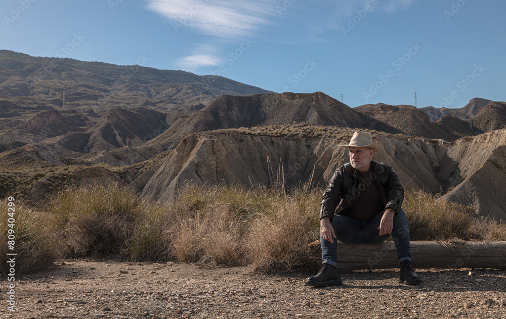 Adult man in cowboy hat siting on tree trunk on wild Adult man in cowboy hat siting on tree trunk on wild