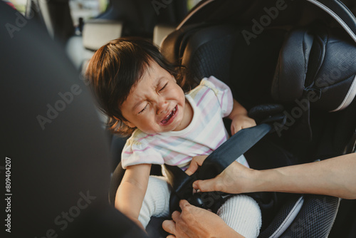 mother is fastening safety belt to crying toddler girl in car seat, safety baby chair travelling