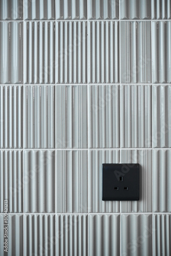 A black electrical outlet mounted on a textured white tiled wall
