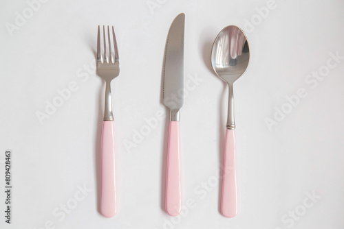 a pink fork  knife and spoon on a white surface