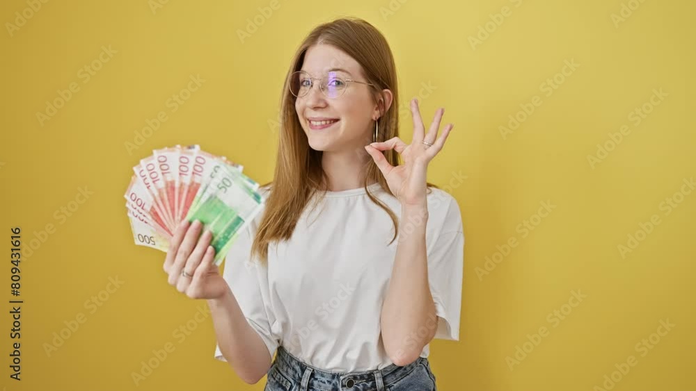 A content caucasian woman displays norwegian kroner notes against a yellow isolated background, signifying financial concepts. A content caucasian woman displays norwegian kroner notes against a yellow isolated background, signifying financial concepts.