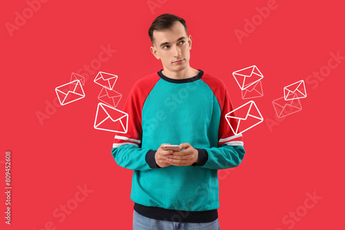 Young man with mobile phone messaging on red background photo
