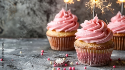  Three cupcakes, each topped with pink frosting and sprinkles, feature a sparkler on top
