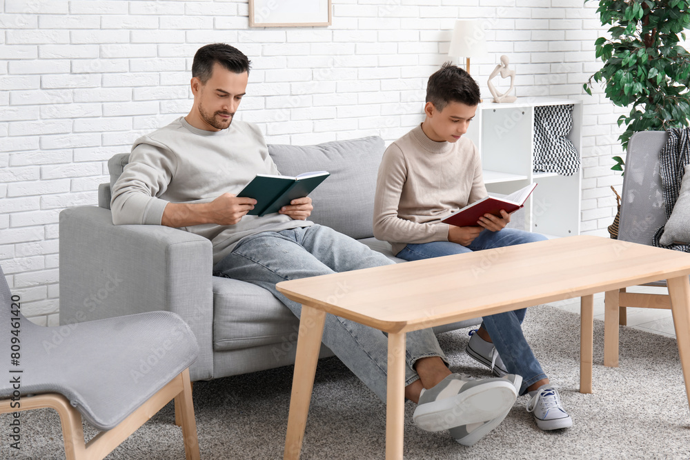 Father and his little son reading books on sofa at home Father and his little son reading books on sofa at home