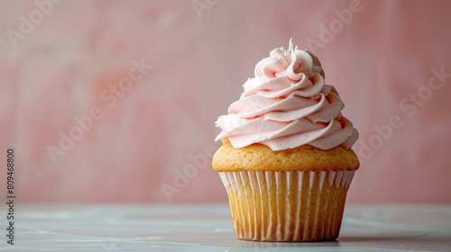   A tight shot of a cupcake, adorned with frosting, atop a pristine white table Behind it, a pink wall forms the backdrop