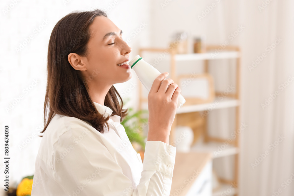 Happy young woman drinking tasty yoghurt in kitchen Happy young woman drinking tasty yoghurt in kitchen