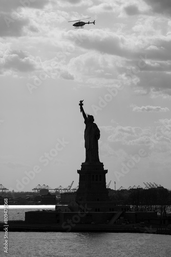 Monochrome image Statue of Liberty as seen from ship in harbor with frewight cranes in background