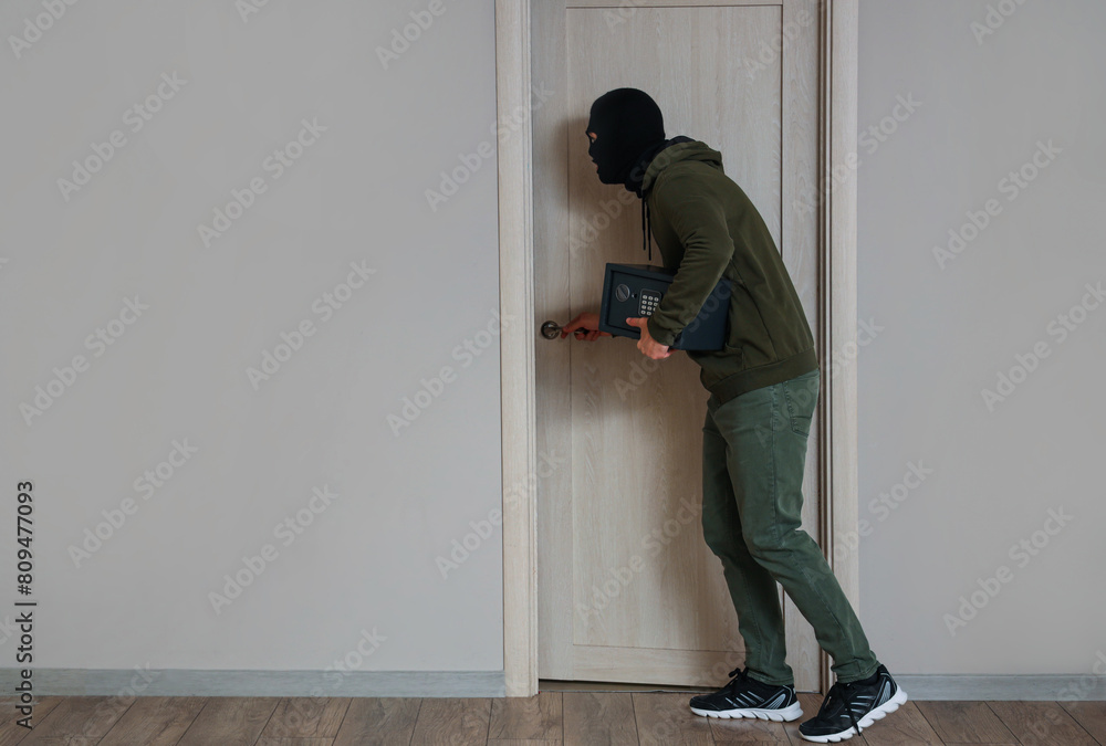 Male thief stealing safe at door in room Male thief stealing safe at door in room