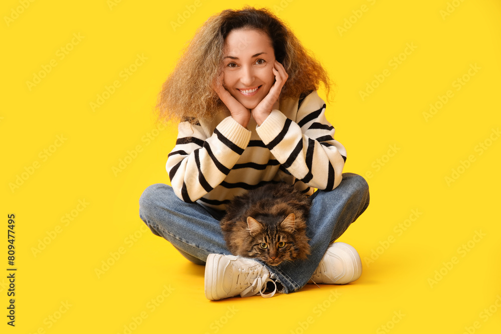 Mature woman with cute cat sitting on yellow background
