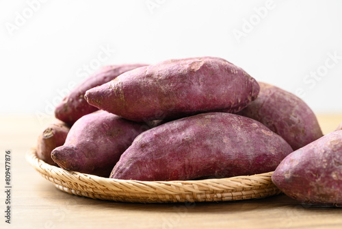 Raw purple sweet potatoes in basket on wooden table with white background, Food ingredient