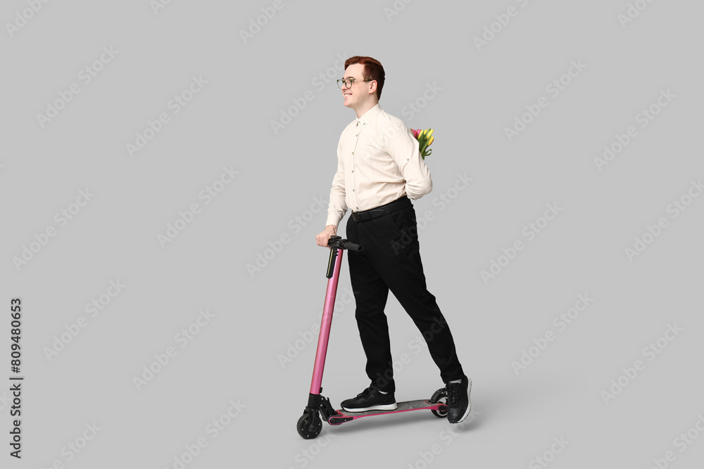 Young man with modern electric kick scooter and bouquet of beautiful tulips on grey background Young man with modern electric kick scooter and bouquet of beautiful tulips on grey background