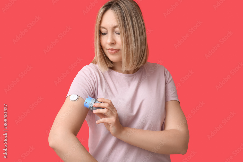 Woman with glucose sensor for measuring blood sugar level and applicator on red background. Diabetes concept Woman with glucose sensor for measuring blood sugar level and applicator on red background. Diabetes concept