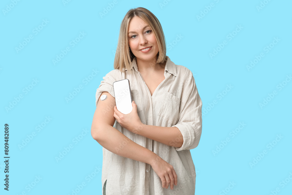 Woman with glucose sensor for measuring blood sugar level and phone on blue background. Diabetes concept Woman with glucose sensor for measuring blood sugar level and phone on blue background. Diabetes concept