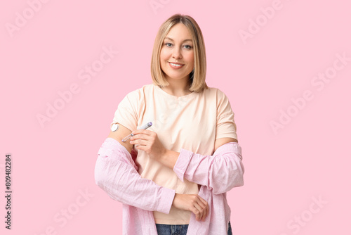 Woman with glucose sensor for measuring blood sugar level and lancet pen on pink background. Diabetes concept