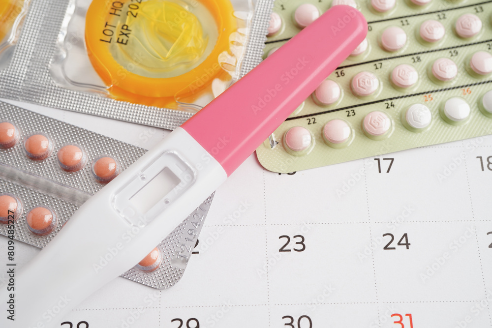 Pregnancy test with birth control pills and condom for female on calendar, ovulation day. Pregnancy test with birth control pills and condom for female on calendar, ovulation day.
