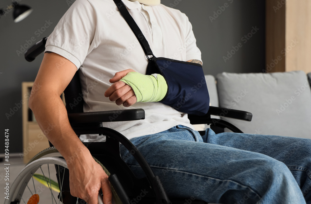 Injured young man with broken arm in wheelchair after accident at home, closeup Injured young man with broken arm in wheelchair after accident at home, closeup