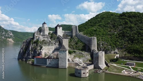 Drone footage over the Danube River showing the Golubac Fortress with a green mountain and blue sky photo