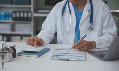 A professional and focused Asian female doctor in scrubs is working and reading medical research on her laptop in her office at a hospital.