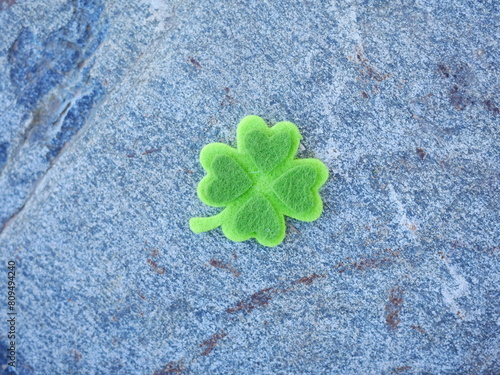 A green clover is sitting on a grey rock