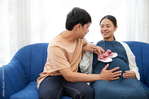 pregnant woman with her husband showing small shoes on stomach for newborn baby