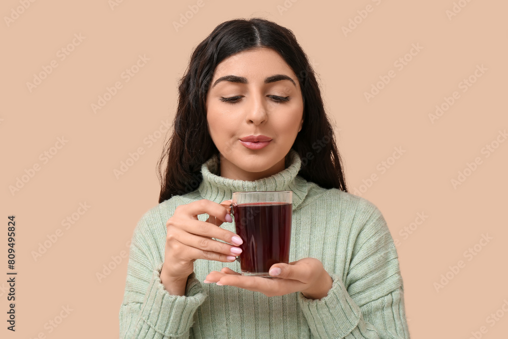 Beautiful young woman with glass cup of hot tea on beige background Beautiful young woman with glass cup of hot tea on beige background